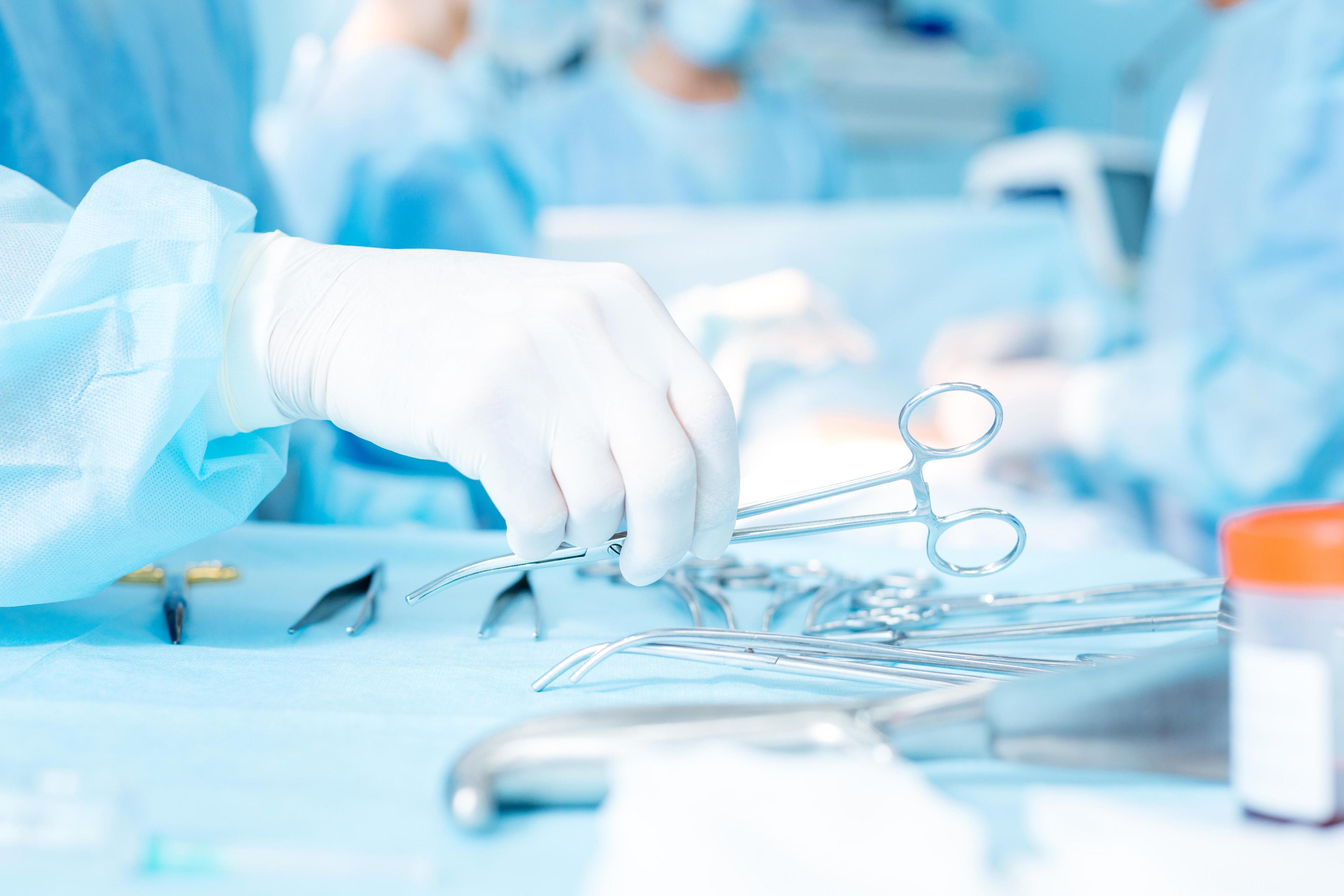 A hand reaching for forceps during an operation.